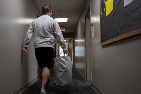 Student walking with laundry in dorm.